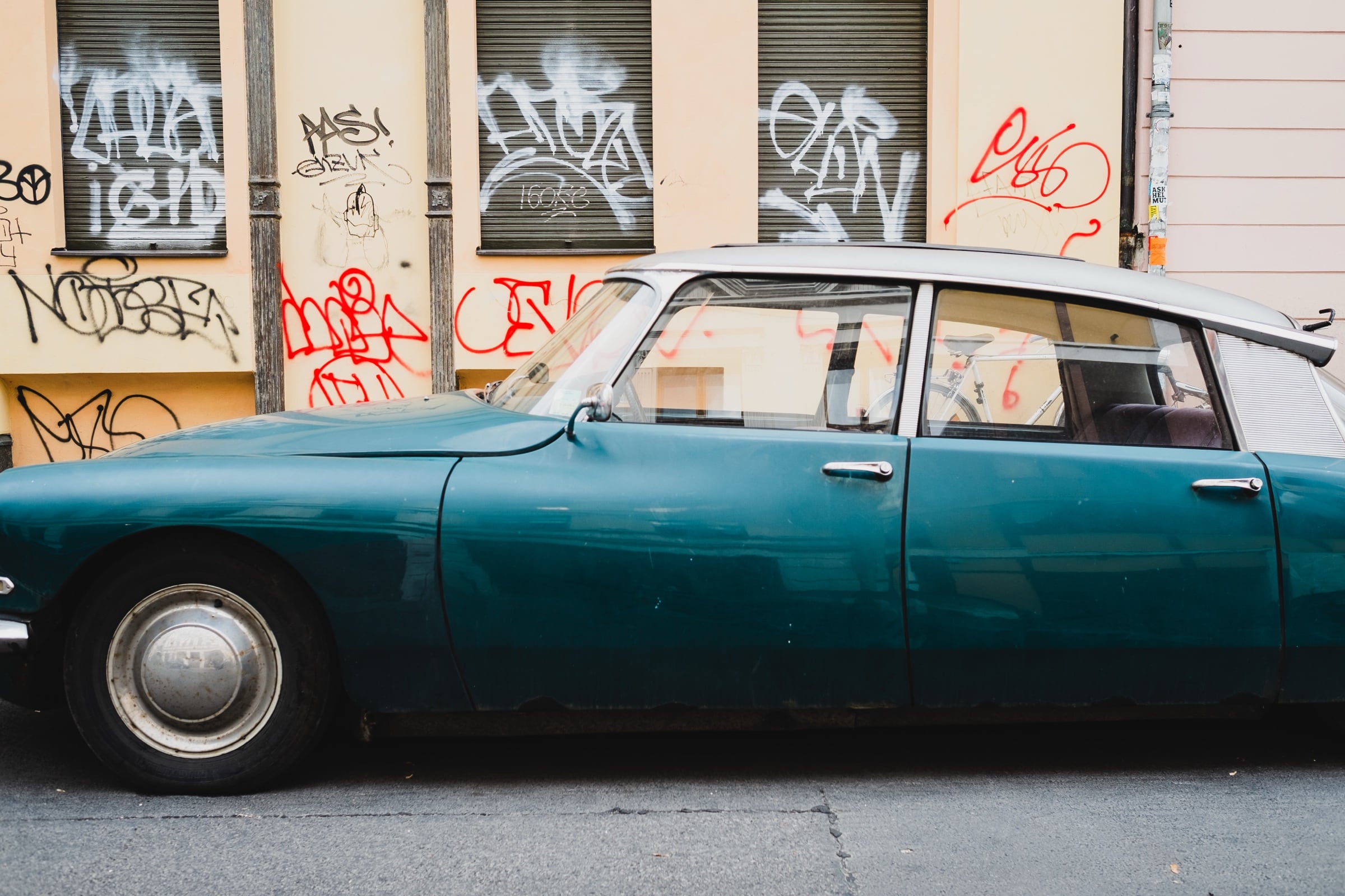 Tyrkysový historický automobil před zdí s graffiti